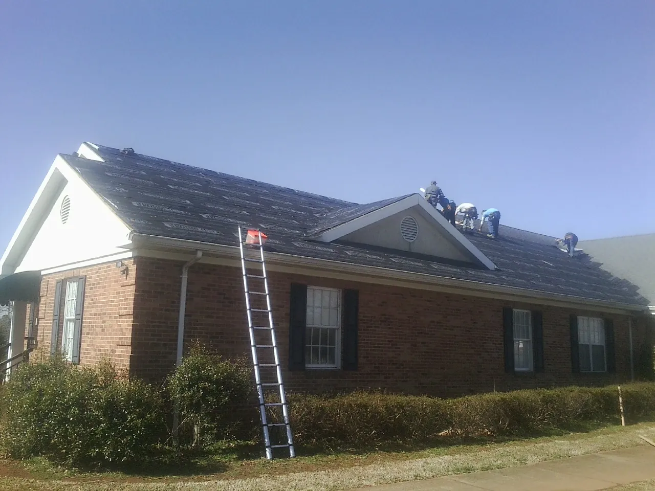 Crew tearing shingles off a brick ranch roof with a ladder set — Metal Roof Repair work by our crew in Mission Viejo