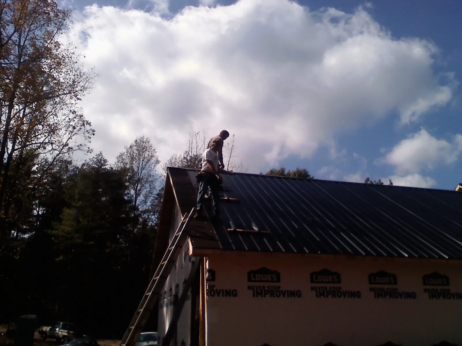 Roofer fastening dark metal panels high against a cloudy sky, from a Roof Inspection job in Mission Viejo