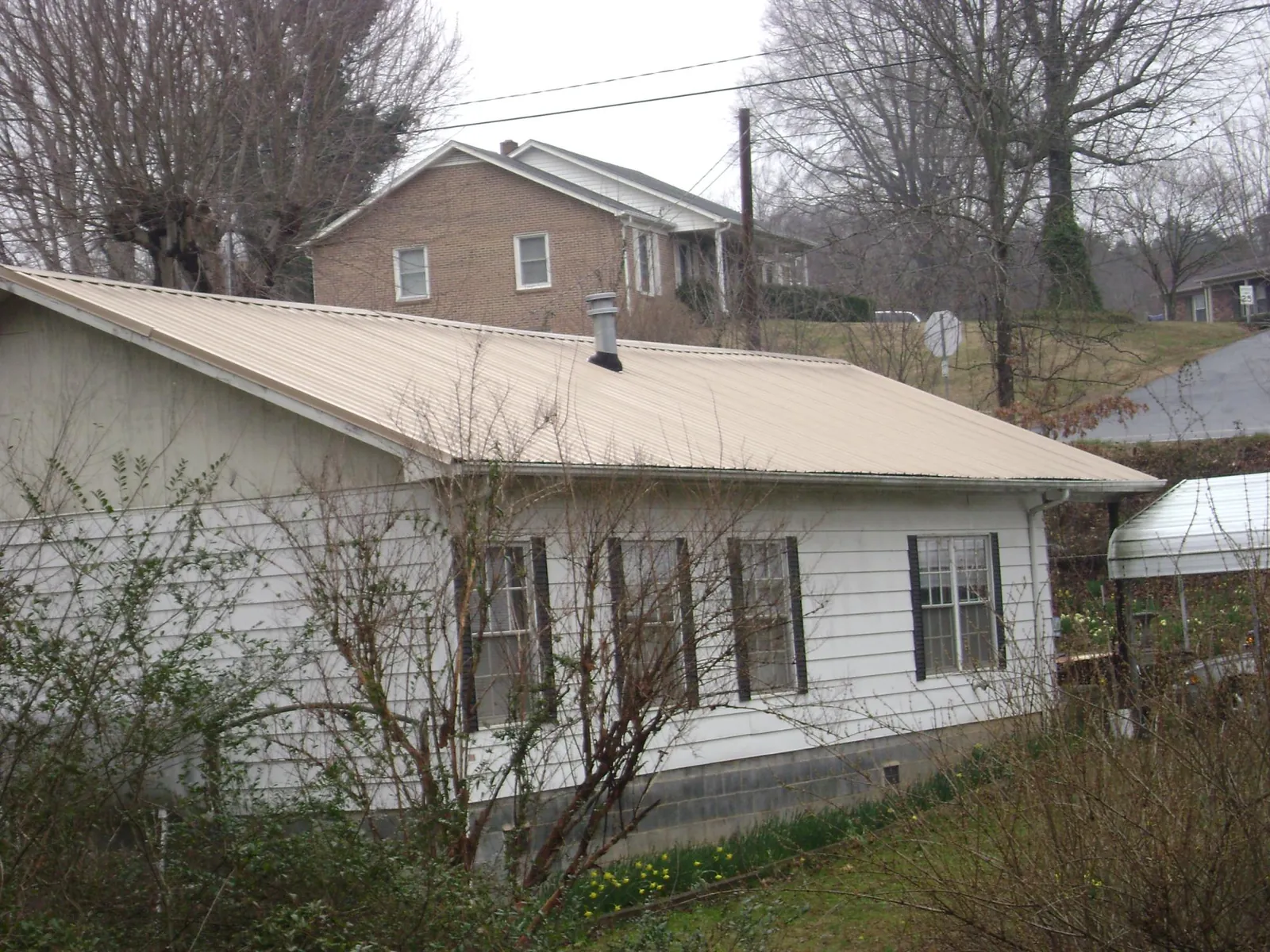 Tan metal roof on a white sided house set into a hillside — Commercial Roofing by Roofing Brothers in Mission Viejo